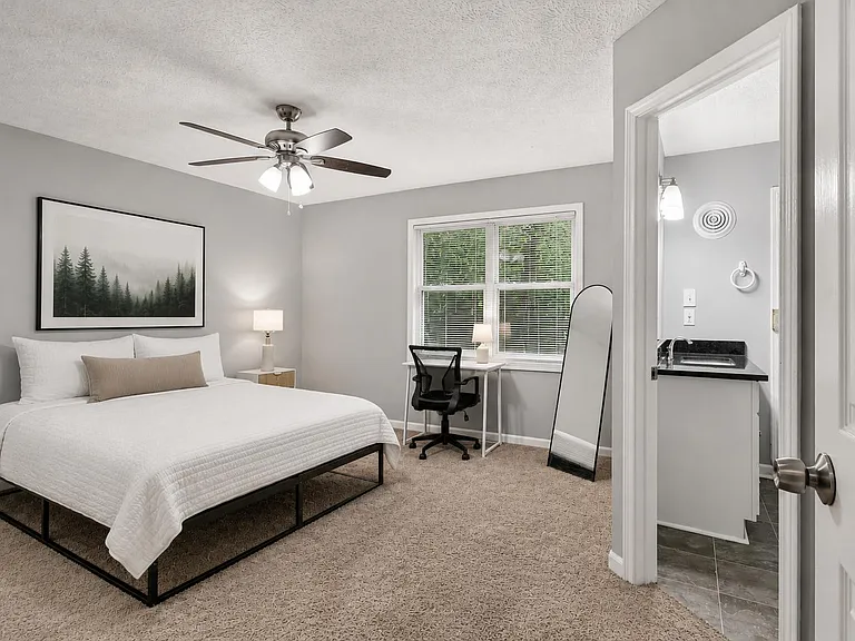 Primary bedroom with a ceiling fan, large window, workspace, large walk in closet, and an en-suite bathroom.