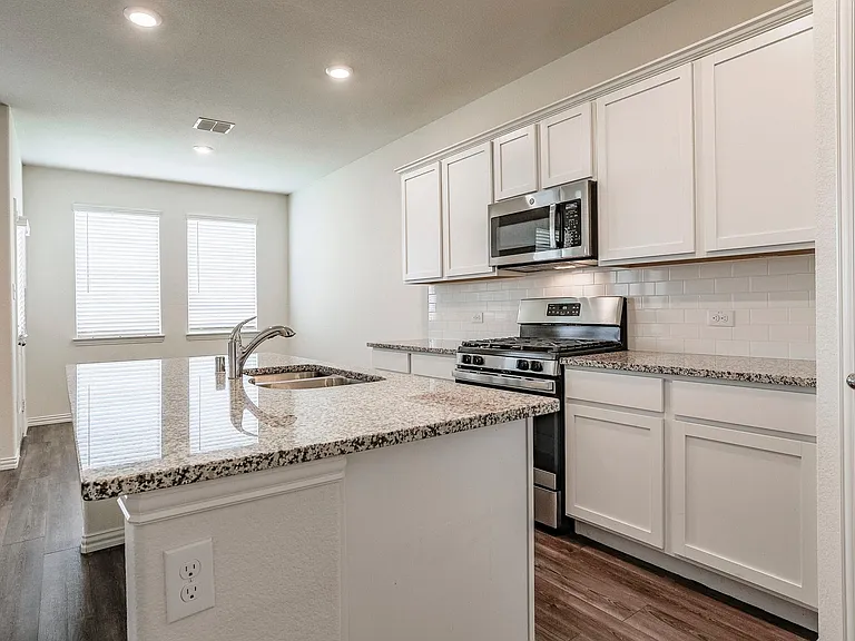 Kitchen featuring sink, appliances with stainless steel finishes, dark hardwood / wood-style floors, white cabinets, and a center island with sink