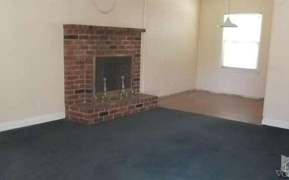 Living room sports attractive brick fireplace with raised hearth & mantle.  View into dining area at end of kitchen.