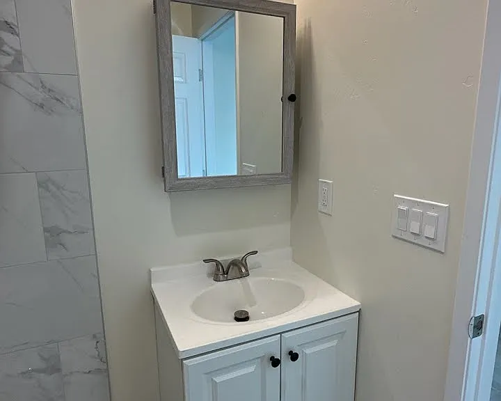 Modern bathroom featuring a stylish white vanity with integrated storage, a mirrored medicine cabinet, and contemporary lighting. Complemented by durable hardwood-style flooring for a clean and refreshed look.