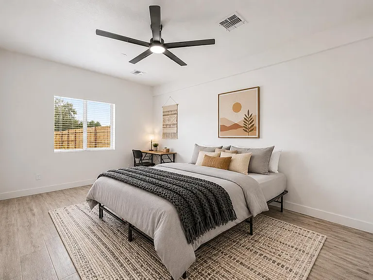 Spacious bedroom with a large window, ceiling fan, and a dedicated desk areaideal for relaxing and working from home.