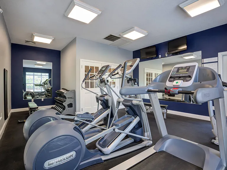 Free weights with bench, cardio equipment and TVs in mirrored 24 hour fitness center.