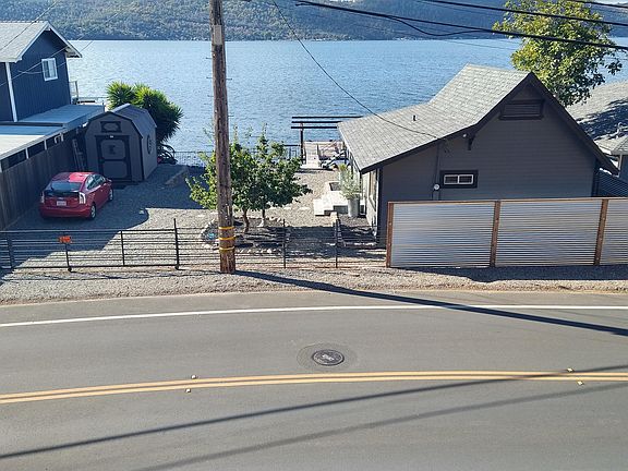 View of the house from above showing the property, parking area and fence around the property and the lake beyond.