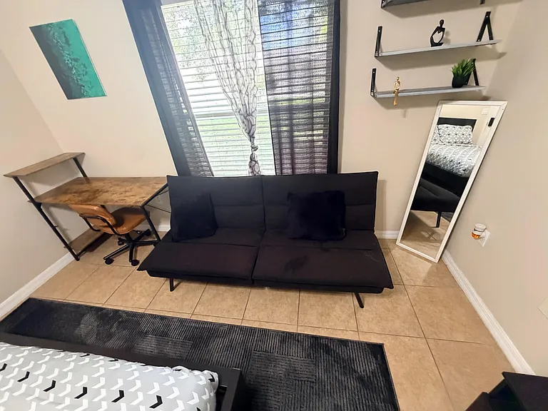 Multi-use bedroom area with a desk workspace, full-length mirror, and window with blinds for adjustable natural light.