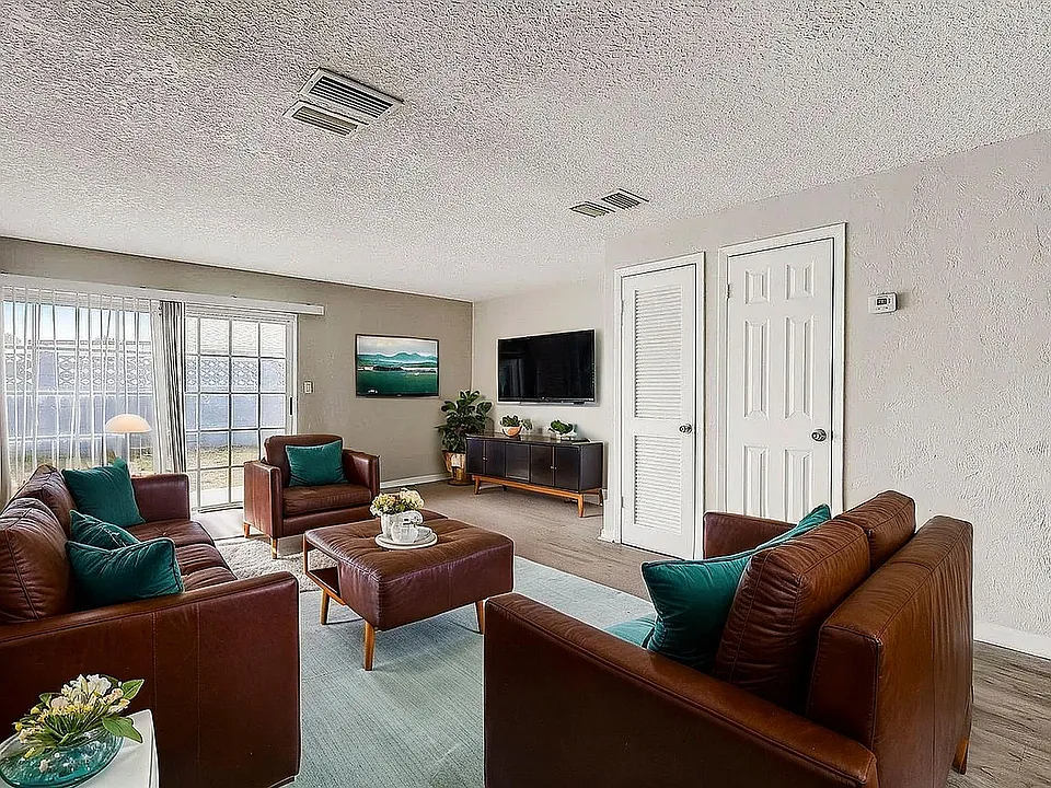 Inviting living room with plush brown leather sofas, vibrant teal cushions, and abundant natural light from large sliding doors.