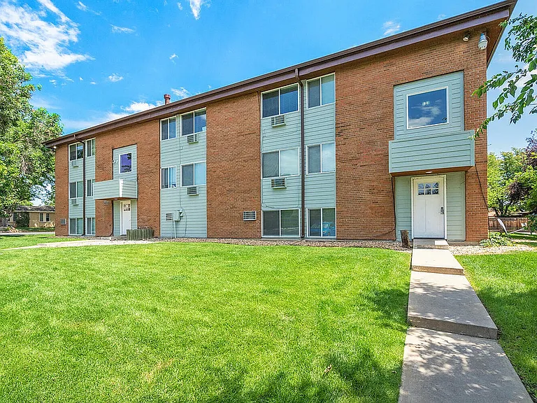 Charming brick apartment complex with modern siding, surrounded by lush green lawn under a bright blue sky.
