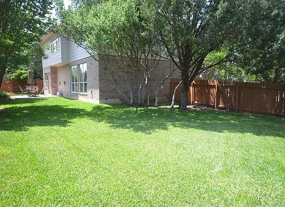 Pleasant back yard with large trees, stained fence, and sprinklers all around the house.