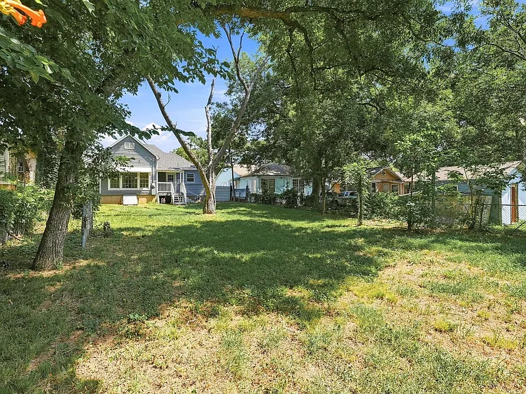 Expansive green space featuring mature trees and a chain-link fence