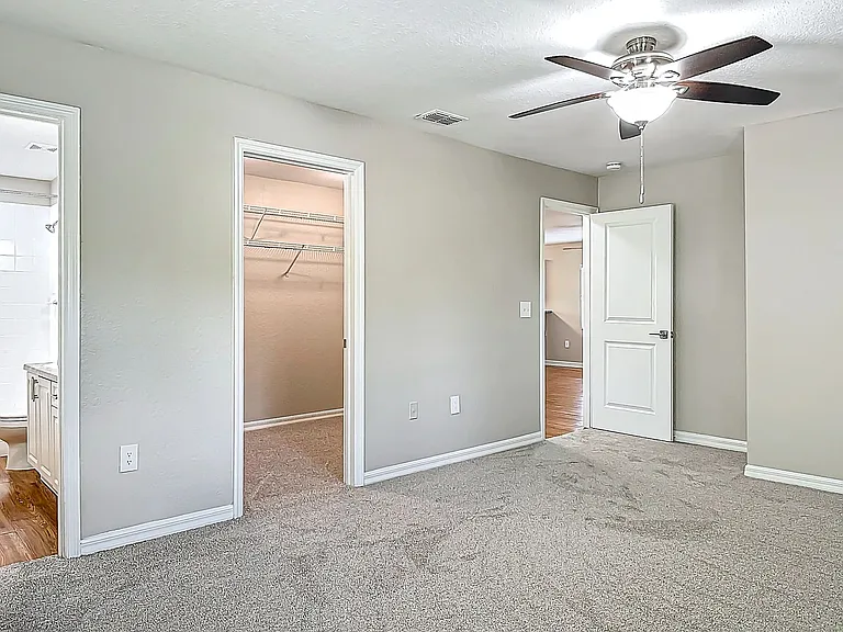 The master bedroom features a modern ceiling fan, plush carpeting, and easy access to both a large walk-in closet and a private en-suite bathroom.