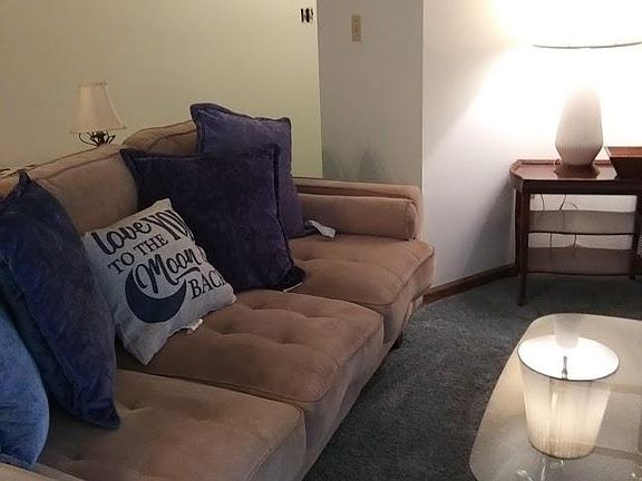 Cozy living room with couch and lots of pillows, coffee table, wooden rocker, end table and lamp.