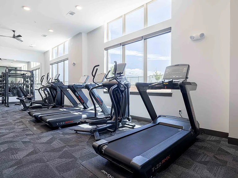 The fitness center at Garrett Parker offers a row of PMX treadmills and an elliptical positioned along floor to ceiling windows for natural light while training.