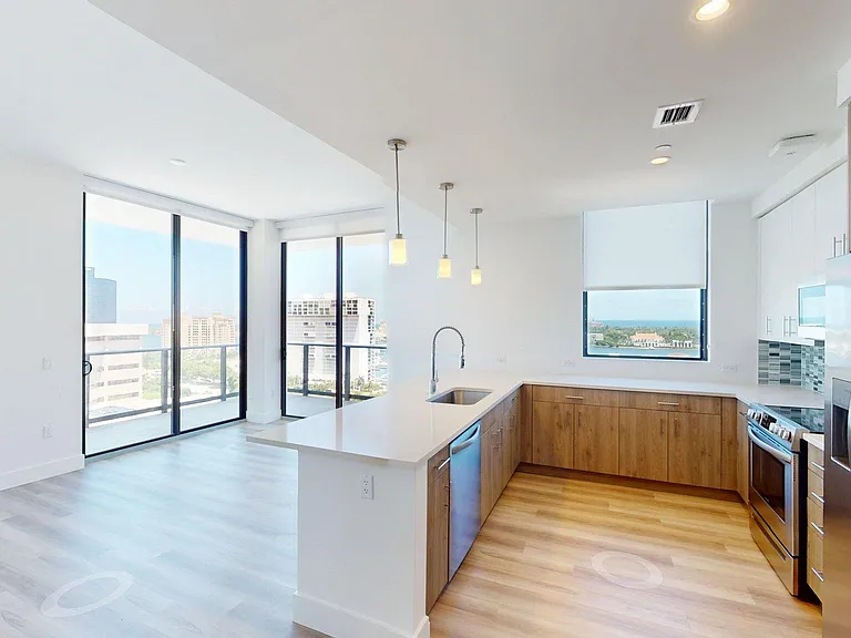 Apartment Kitchen with Stainless Steel Appliances, Dining and Living Room with wood flooring and Balcony.