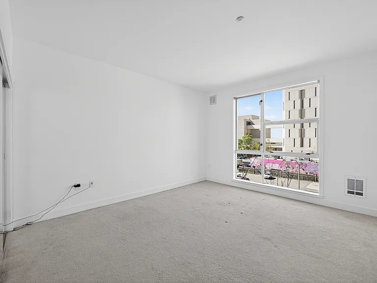 Spacious bedroom with large window, freshly painted white walls, professionally cleaned carpet, and city-facing views.