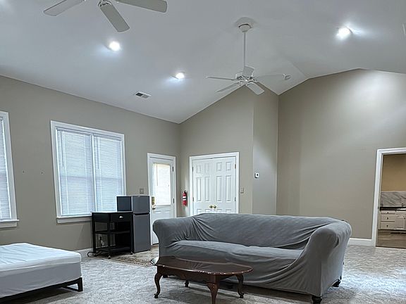 Furnished bedroom with a cozy sofa, coffee table, and ceiling fans for comfort, plus ample natural light from multiple large windows.