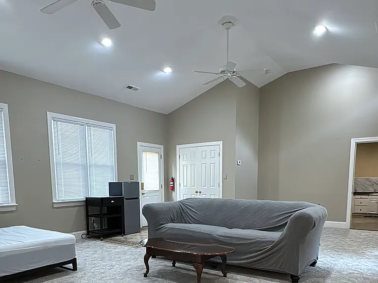 Furnished bedroom with a cozy sofa, coffee table, and ceiling fans for comfort, plus ample natural light from multiple large windows.