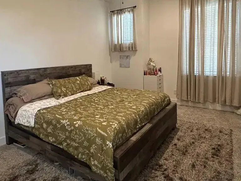 Spacious bedroom with a large bed, plush carpeting, and dual windows with curtains for natural light and privacy.
