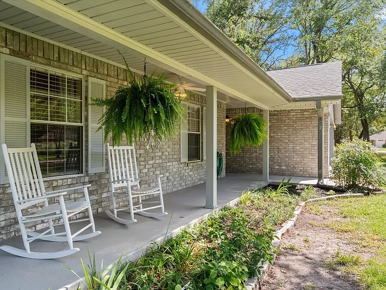 Brick exterior with a covered front porch, featuring a gray concrete surface, light-colored brick facade, and gray louvered shutters