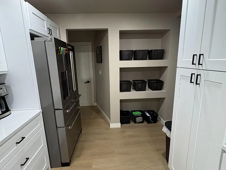 Efficient kitchen corridor with tall shaker cabinetry, stainless French-door fridge, and built-in open shelving storage.