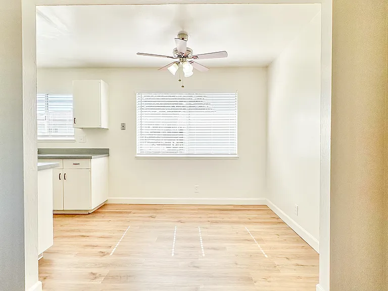 an empty living room with a ceiling fan and a kitchen
