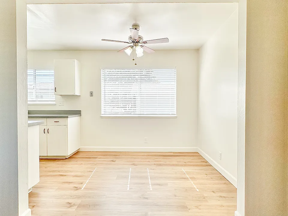 an empty living room with a ceiling fan and a kitchen