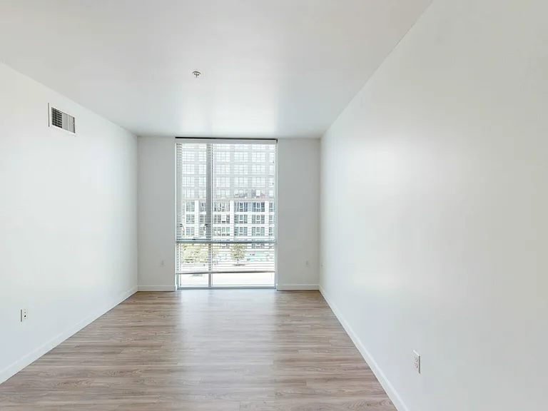 Spacious apartment bedroom with wood-style flooring and floor-to-ceiling windows.
