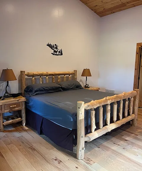 Master bedroom ( has a bathroom). King size bed . It's a big room with a walk in closet. All log furniture... has nightstands and a dresser with 9 drawers. Lamps included and metal wall art piece. Faces front porch entrance. High vaulted ceiling in here.