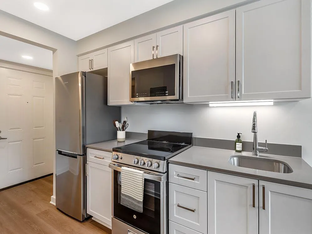 Renovated Package II kitchen with stainless steel appliances, light grey quartz countertops, white shaker cabinetry, and hard surface flooring - eaves Thousand Oaks