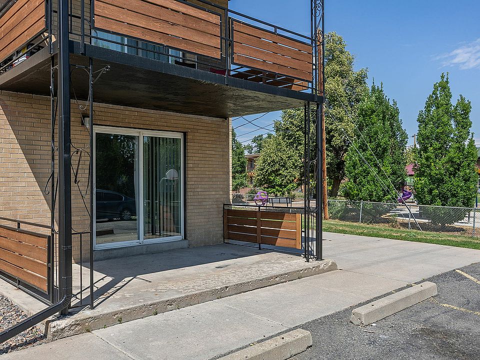 Inviting apartment entrance with modern wooden railing and a spacious patio, nestled in a lush green neighborhood.