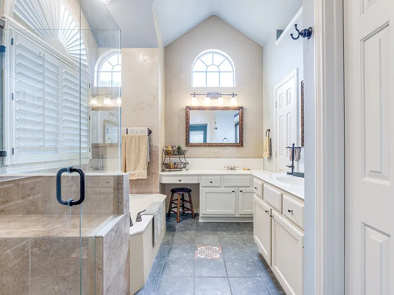 Primary bathroom with lots of natural light, plantation shutters, separated vanities, separate garden tub and a frameless shower.