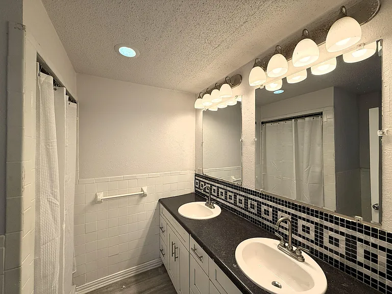 Bathroom with a long double-sink vanity, wide mirror, and tiled tub/shower surround for easy daily routines.