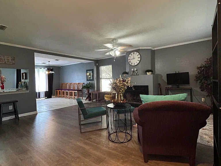 Open living area with wood-style flooring, ceiling fan, and flexible seating, flowing into an adjacent dining space.