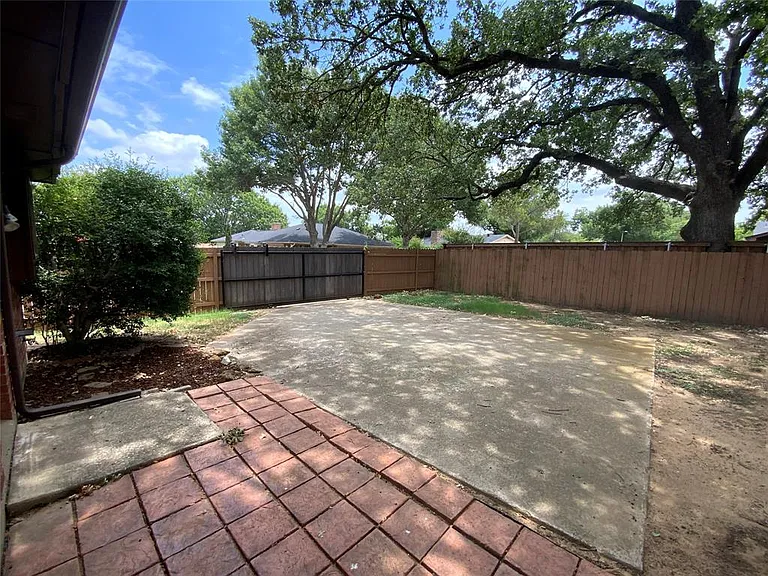 Expansive outdoor space featuring a large concrete patio, a stamped brick patio area, mature trees, and a wooden privacy fence