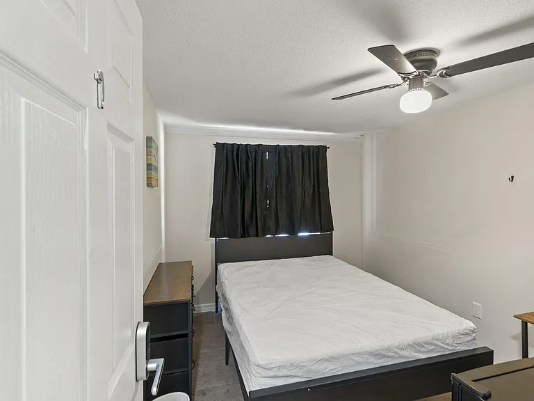 Private bedroom featuring a queen size bed, ceiling fan with light, and a window with blackout curtains for added privacy.