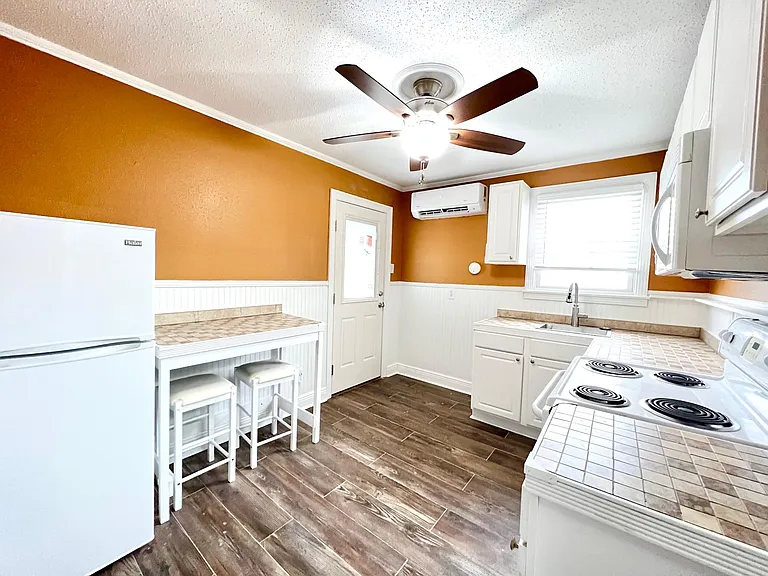 Spacious Kitchen includes refrigerator, electric range, SS single basin sink with gooseneck faucet, cabinets, custom tile counters, niche' shelving, wood plank tile floors and built in dining table!