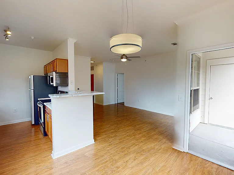 Apartment kitchen with stainless steel appliances, dining and living room with wood-style flooring.