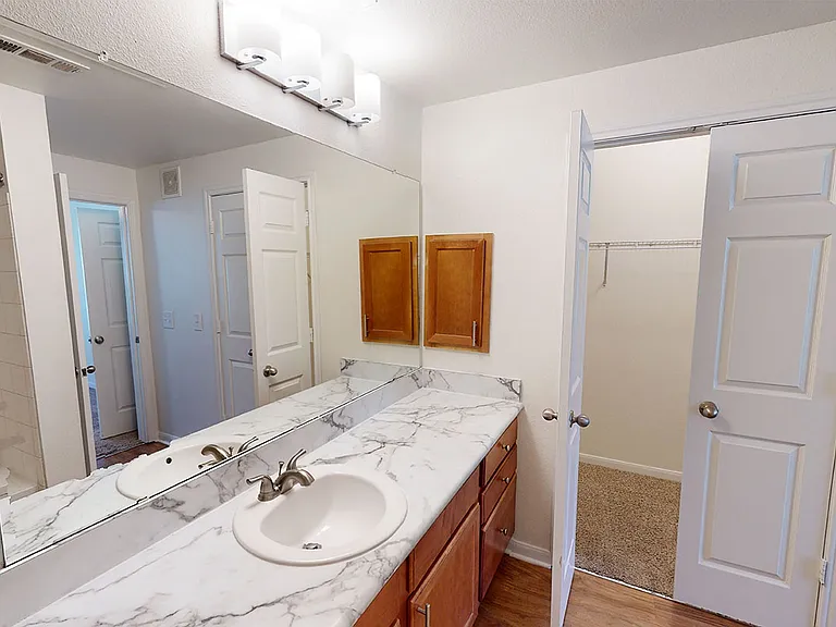 Apartment bathroom with wood-style flooring and marble-style countertops (shown here). Quartz-style countertops are available in select homes.