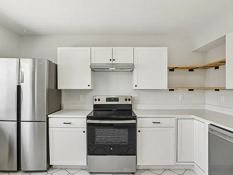 Modern kitchen with sleek stainless steel appliances, white cabinetry, and open wooden shelving.