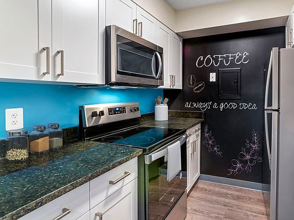 Renovated Package II kitchen with new white cabinetry, granite countertops, stainless steel appliances, painted backsplash, chalkboard accent wall, upgraded lighting and fixtures, and hard surface flooring