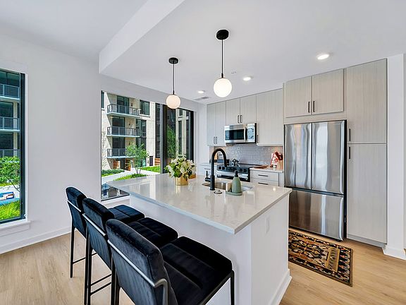 Kitchen with white island, stainless appliances, black barstools, pendant lights, and large windows and stainless steel appliances
