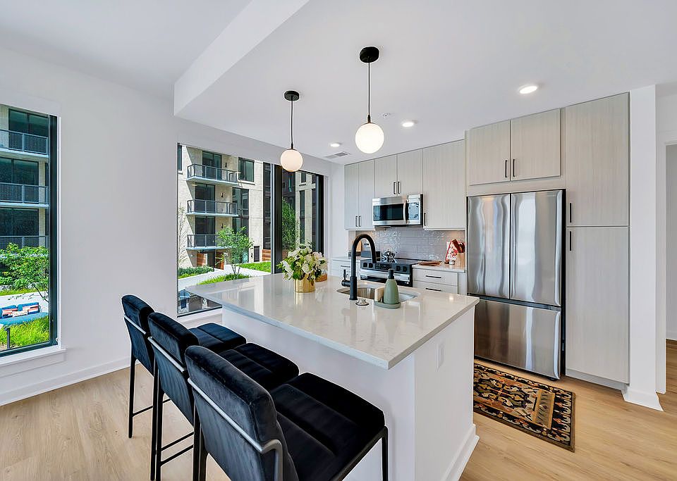 Kitchen with white island, stainless appliances, black barstools, pendant lights, and large windows and stainless steel appliances
