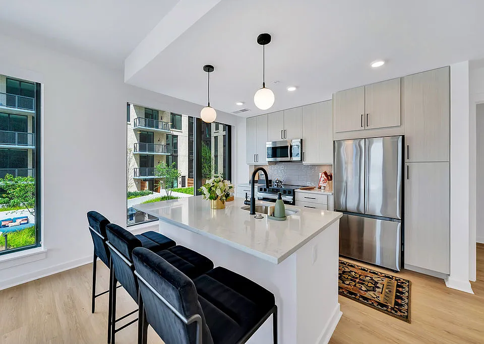 Kitchen with white island, stainless appliances, black barstools, pendant lights, and large windows and stainless steel appliances