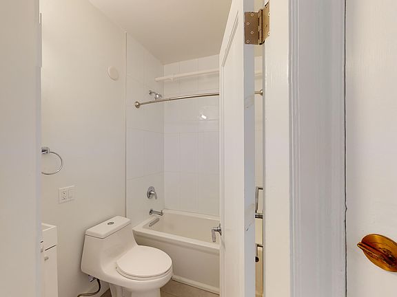 Compact bathroom with walls features a toilet next to a bathtub with shower. The open door highlights a simple, clean design.