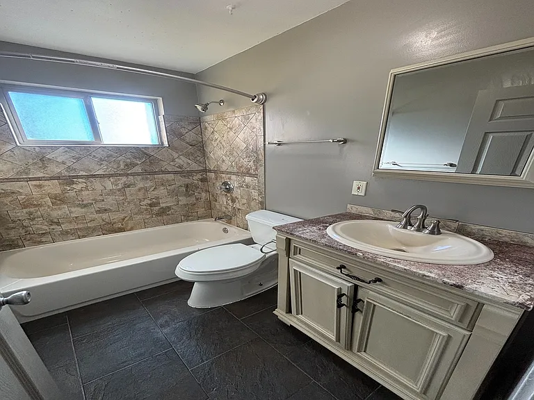 Elegant bathroom with stylish tile accents, featuring a full bathtub, modern vanity, and natural light from a wide window.