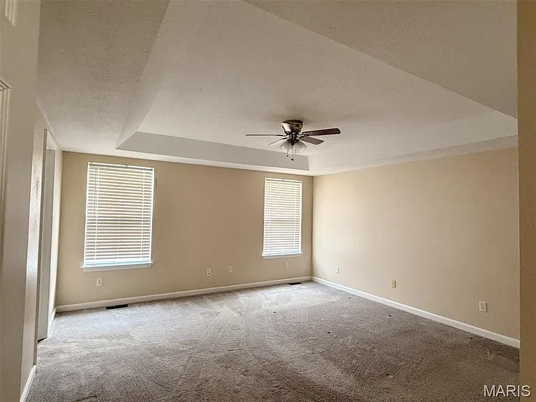 Tray ceiling with a ceiling fan, two windows with blinds, and neutral tone walls
