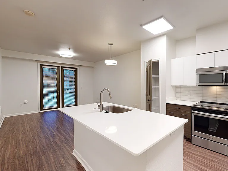 Apartment kitchen with stainless steel appliances, dining and living room with wood-style flooring.
