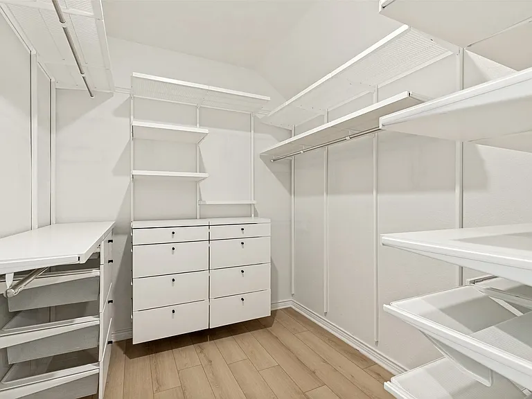 Custom closet system featuring light wood-finish flooring, white built-in shelving, hanging rods, an integrated dresser with six drawers, and a folding surface