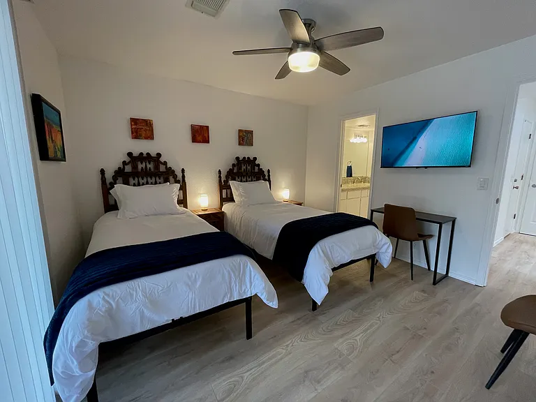 Secondary Bedroom in 2 twin XL bed configuration. En suite bathroom, access to downstairs patio, Roku TV, workspace and 2 chairs.