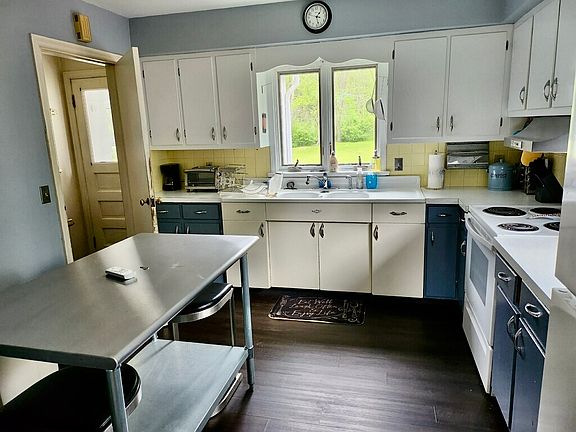 Kitchen with original cast-iron double sink and cabinet overlooking large backyard and woods. To the left, door to back porch and to stairs leading to the basement to the washer and dryer.