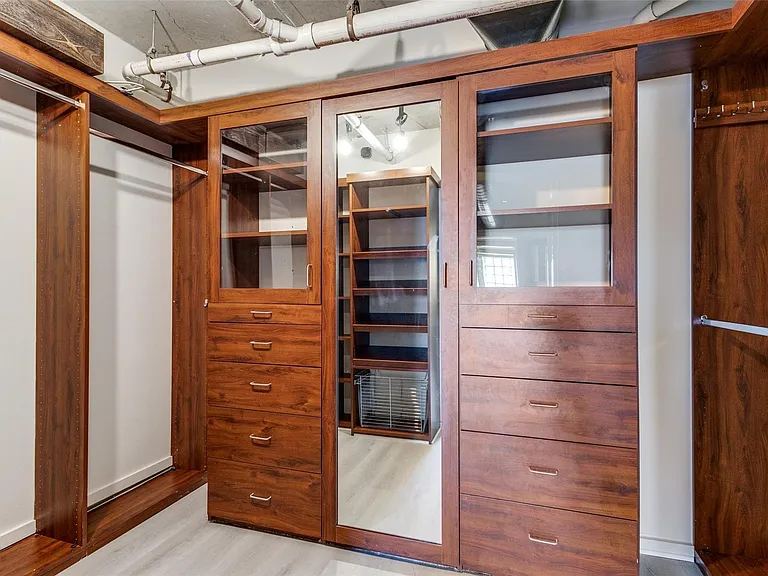 Custom wood-finish closet system featuring integrated drawers, glass-front cabinetry, mirrored panels, and ample hanging space
