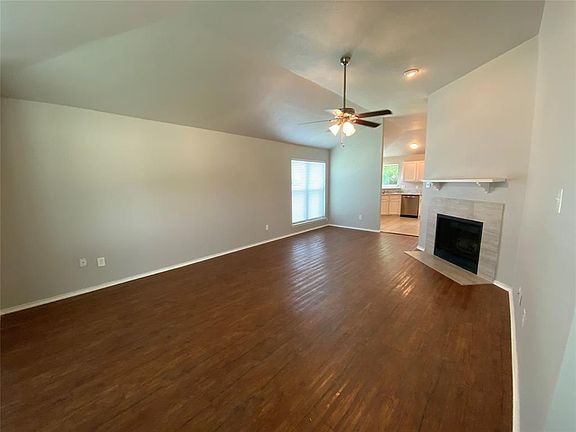 Spacious living area featuring wood-finish flooring, a vaulted ceiling, and a fireplace with a tile surround and mantel